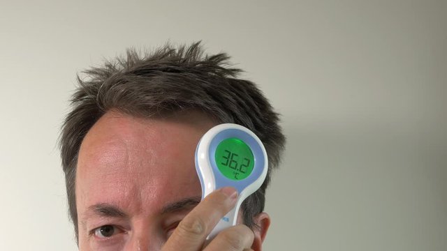 Man Takes Temperature With Digital Thermometer On Forehead