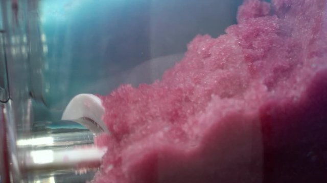 Ice cold sorbet machine mixing fruit juice. Freezing slush spinning around, summer treat. Crushed iced coloured with fruit flavor sweeteners