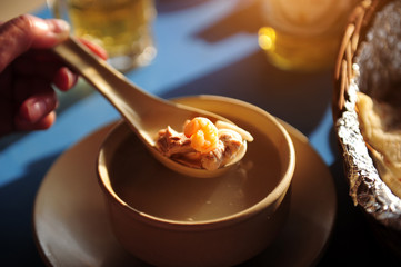 Hand holding a spoon with a shrimp and a piece of boiled fish, close-up. Seafood soup at the beach cafe. Diet soup with seafood.