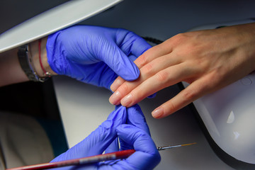 Manicure master in gloves apply base coat to the client's nails. Manicure in the salon, close up. Beauty and care of hands.