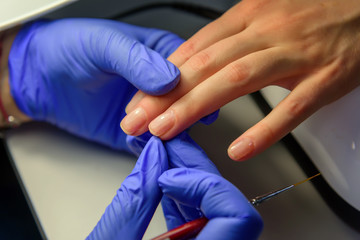 Manicure master in gloves apply base coat to the client's nails. Manicure in the salon, close up. Beauty and care of hands.