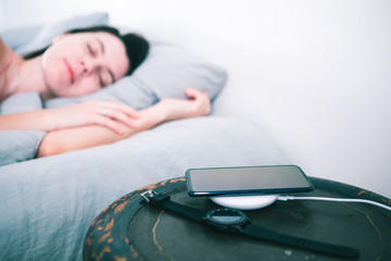sleeping woman in bed cellphone charging on wireless charger