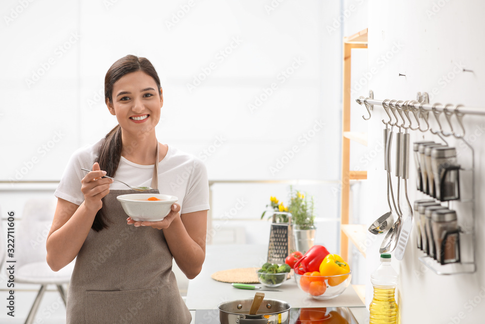 Wall mural young woman eating tasty vegetable soup in kitchen