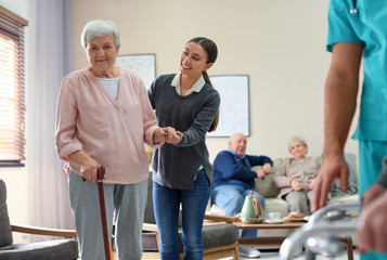 Care worker helping to elderly woman with stick in geriatric hospice
