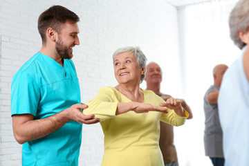 Obraz premium Care worker helping elderly woman to do sports exercise in hospital gym.