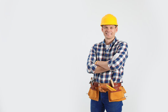 Handsome carpenter with tool belt on light background. Space for text