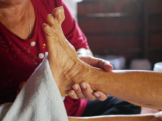 Hands of a woman holding an older person's feet, while gently wiping / cleaning it with a wet...