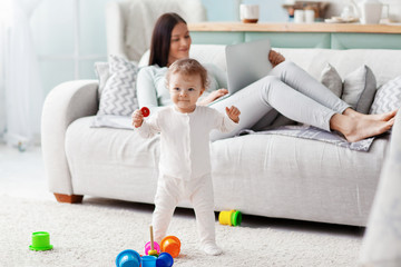 Mom works at a laptop at home while her child is playing. Business and family concept.