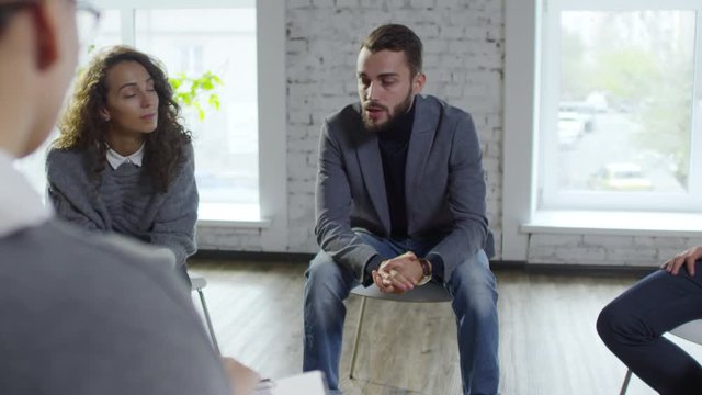 Medium shot of successful businessman with beard talking and sharing problems on support group meeting