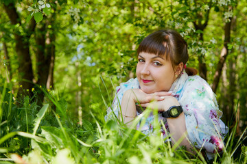 Portrait of an ugle fat chubby plump girl lying in grass and blossoming apple tree with white flower background in the park in a spring time