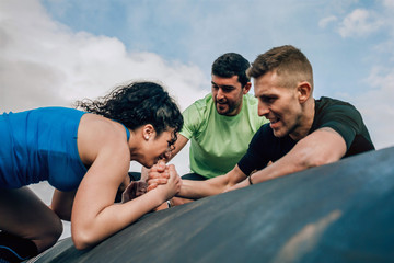 Female participant in an obstacle course climbing a drum helped by her teammates