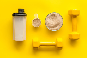 Sport nutrition. Whey protein, shaker, dumbbells on yellow background top-down flay lay