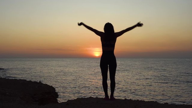 Young adult girl standing near sea, looking at sunset