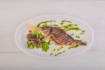 whole baked fish with brussels sprouts, pesto sauce on a white wooden background