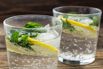 Two glasses of lemonade with lemon, mint and ice cubes on wooden background. Summer drink