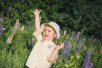 Portrait of a little girl in a hat in a field of flowers. Field of Lupins. Summer