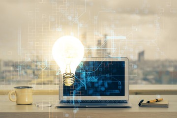 Computer on desktop in office with bulb icon hologram. Multi exposure. Concept of idea.
