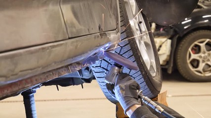 Expert technician using an angle grinder to repair the damage to a car body in the woorkshop with sparks flying - Powered by Adobe