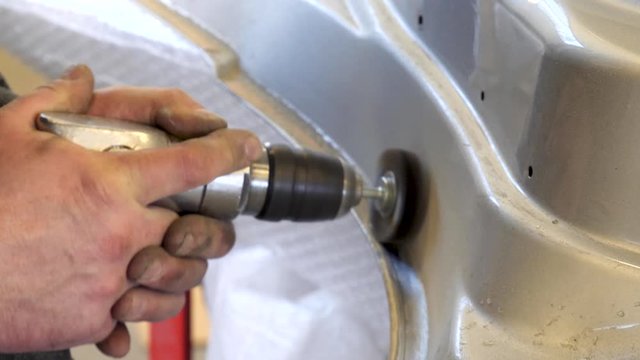 Cleaning up a car body part with a wire brush on a rotary tool before painting after a collision repair at an auto body shop