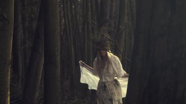 Woman in white with headdress emerges from ominous forest. Slow motion