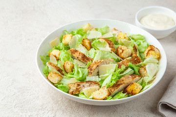 traditional Caesar salad with lettuce, roasted chicken,  croutons and cheese in white bowl