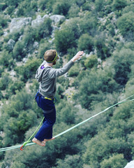A man is walking along a stretched sling. Highline in the mountains. Man catches balance....
