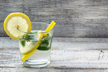 Water with lemon and mint in a glass on wooden background. Summer fresh lemonade drink