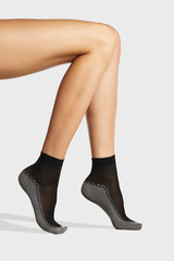 Cropped shot of female legs in the black nylon socks with gray cotton bottoms and zigzag stripe. The photo is made on the light-gray background.  
