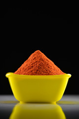 Red chili powder in yellow bowl on dark background