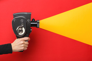 Female hand holding old style film movie camera imitating shooting process on a red background - obrazy, fototapety, plakaty