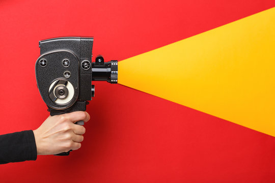 Female hand holding old style film movie camera imitating shooting process on a red background