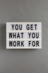 'You get what you work for' words on a modern board on a gray background, top view. Overhead, from above, flat lay.