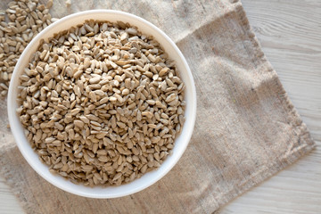 Raw Sunflower Seed Kernels in a white bowl on a white wooden background, top view. Copy space.