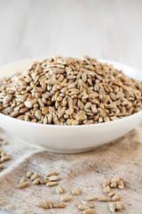 Raw Sunflower Seed Kernels in a white bowl on a white wooden surface, side view. Close-up.