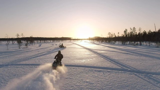 Sunrise drone shot of two adventurers riding curves on snowmobiles in Lappland, Sweden