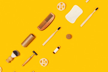 Ecological accessories for body care: natural sponges, wooden comb, shaving brush, glass bottle with lotion, soap, toothbrushes and craft tube located on tricolor yellow background.