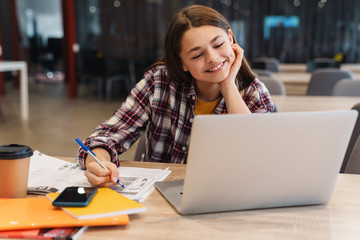 Image of smiling girl doing homework with laptop and exercise books