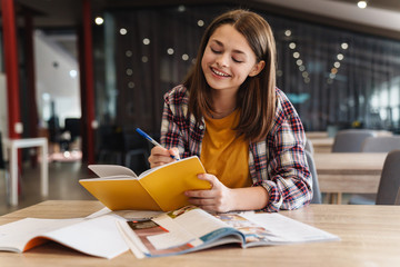 Image of smiling caucasian girl doing homework with exercise books