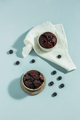 Homemade chocolate beetroot muffins with bilberries in white cake-tins on blue background, white napkin, hard light shot