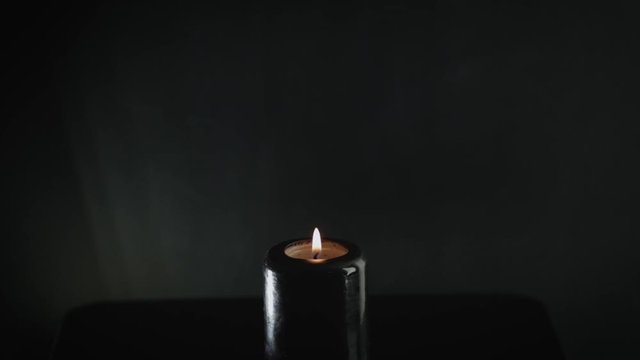 lighting black candle with match on black background, esoteric concept 