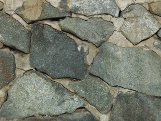 fragment of a wall finished with untreated large natural stone on cement