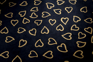 Handmade background of heart shapes stamped in gold on black textured paper
