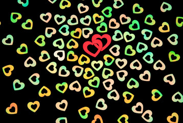 Two red hearts interlocking in a group of colorful iridescent glitter on a black background 