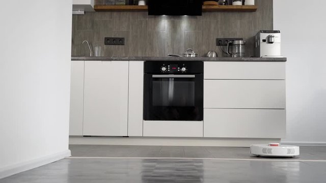 modern kitchen of small apartment with grey and white colors in interior, robotic vacuum cleaner is working