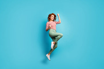 Fototapeta na wymiar Goal. Full size profile photo of funny pretty lady jump high up raise fists winner sports competition wear casual red white shirt green trousers shoes isolated blue color background