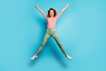 Fototapeta na wymiar I am free. Full body photo of crazy lady jumping high rejoicing weekend sunny day spread hands wear casual red white shirt green trousers shoes isolated blue color background