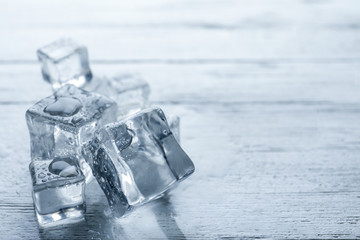 Crystal clear ice cubes with water drops on white wooden table, closeup. Space for text
