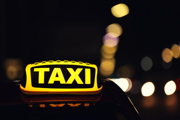 Taxi car with yellow roof sign on city street at night, closeup