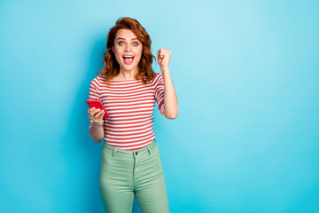 Portrait of delighted shocked woman use cellphone win social media lottery raise fists scream yes wear stylish pullover isolated over blue color background