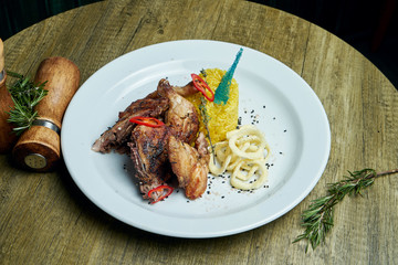 Roasted tapaka chicken with spices and a side dish of rice on a white plate. Georgian cuisine. Close up view on tasty food. Wooden background